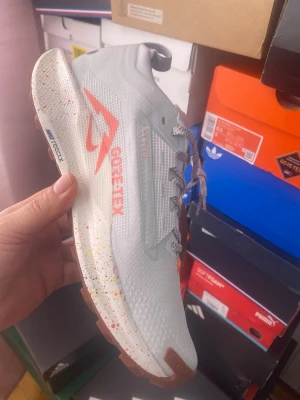 Nike Pegasus Trail 4 GORE-TEX sneakers - Snygga Nike Pegasus Trail 4 GORE-TEX sneakers i ljusgrått med orange detaljer och stänkmönstrad sula. Ovandelen är i mesh med vattentätt GORE-TEX-material och reflekterande detaljer. Perfekta för dig som gillar att sticka ut och vill ha funktionella sneakers för alla väder.