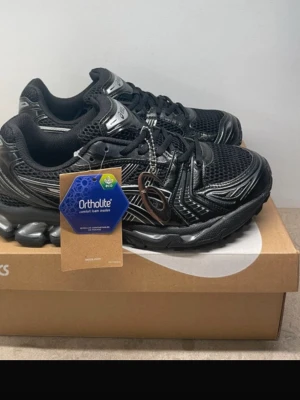 Svarta Asics GEL-Kayano 14 sneakers - Svarta Asics GEL-Kayano 14 sneakers med coola detaljer i silver och meshpaneler för extra andningsförmåga. Skorna har Ortholite innersula och en chunky sula med GEL-dämpning för maxad komfort. Perfekta för dig som gillar sportig och trendig stil.