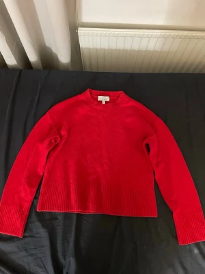 Röd stickad tröja med ribbade detaljer - En snygg röd stickad tröja med rund hals och breda ribbade muddar vid ärmslut och nederkant. Tröjan har en rak passform och är perfekt för att hålla värmen under kyliga dagar. Enkel och stilren design som passar till det mesta.