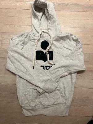 Grå hoodie från Isabel Marant - Snygg ljusgrå hoodie från Isabel Marant med stor svart logga och text på bröstet. Viss avskavd på trycken men annars fint skick.🤍