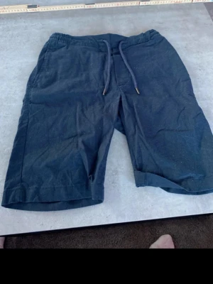 Mörkblå linneshorts Dressmann XS - Säljer ett par mörkblå shorts från Dressmann i linnemix. De har elastisk midja med snörning, två sidofickor och två bakfickor med knapp. Perfekta för varma dagar och riktigt sköna att bära. # Dressman #mode 