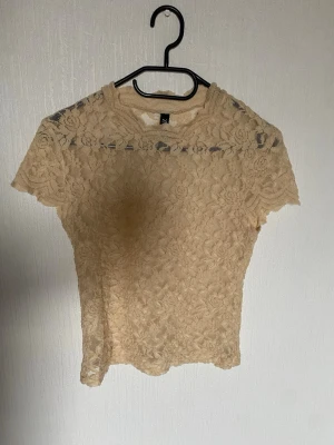 populär beige spetsblus  - Säljer en beige, transparent topp i spets med mönster och korta ärmar. Toppen har figurnära passform och strechtigt material