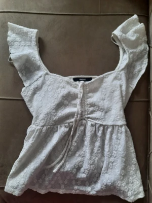 Vit blus med volangärmar från Bik Bok - Supersöt vit blus från Bik Bok med volangärmar och knyt framtill. Blusen har en lätt strukturerad yta och är perfekt för en somrig look. Den har en feminin passform och är tillverkad i ett mjukt material. 