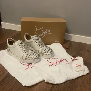 Christian Louboutin sneakers vita  - Säljer ett par vita sneakers från Christian Louboutin i skinn med coola nitar på tån och hälen. De har den klassiska röda sulan och har även kvar originalförpackning och dustbags. Perfekta för att ge din outfit en perfekt touch. Skorna har vissa defekter men inga större eller som stör funktionen Skriv gärna om ni är intresserade ❤️ köptes för ca 11 000
