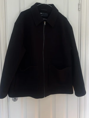 Svart ulljacka från ASOS DESIGN - Stilren svart jacka från ASOS DESIGN i ullblandning. Jackan har klassisk krage, raka linjer, två stora framfickor och dragkedja framtill. Perfekt för dig som gillar minimalistisk och clean stil.