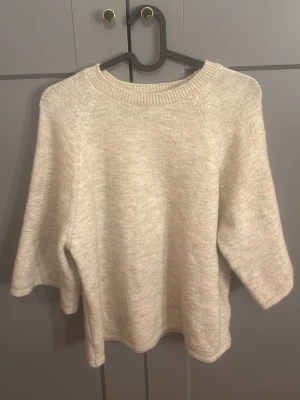 Beige stickad tröja Gina Tricot - Mysig beige stickad tröja från Gina Tricot med rund halsringning och trekvartsärmar. Tröjan har en enkel och stilren design med ribbade detaljer vid halsen. Perfekt för lager på lager och passar till det mesta.