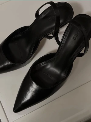 Svarta pumps / sling back pumps NA-KD - Stilrena svarta pumps i skinnimitation från NA-KD med spetsig tå och smal rem runt hälen. Skorna har låg klack och en elegant, minimalistisk design som passar perfekt till många olika outfits. STORLEK 38. Helt oanvända