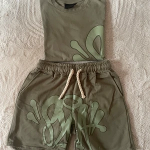 Grönt set från SYNA WORLD - Tvådelat set i ljusgrönt från Duckeries med matchande t-shirt och shorts. Båda delarna har ett stort, abstrakt tryck i en ljusare grön nyans. Shortsen har dragsko i midjan och sidofickor. Perfekt för en avslappnad och trendig stil. Shorts är stl L eftersom annars är dem för små. Tröjan är S