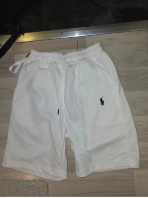 Vita shorts från Polo Ralph Lauren - Snygga vita shorts från Polo Ralph Lauren med klassisk logga broderad på vänster ben. Shortsen har elastisk midja med snörning och två sidofickor. Perfekta för sommaren och riktigt clean stil.