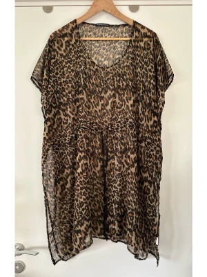 Leopardmönstrad transparent klänning / kaftan - Läcker brun leopardmönstrad kaftan / strandklänning / klänning / tunika från MyWear i one-size. Klassisk modell med v-ringning, korta ärmar och dragsko i midjan för justerbar passform från XS till XL. Halvtransparent lätt, luftig design. Perfekt för en avslappnad men stilfull look. Mycket gott skick, som ny!  Skickas mot porto, kan även hämtas i Stockholm.
