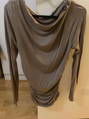 Beige långärmad draperad topp - Trendig beige topp med långa ärmar och snygg drapering både vid halsringningen och midjan. Tunn och stretchig, perfekt för att skapa en cool och avslappnad look. Passar dig som gillar stilrena plagg med en twist.