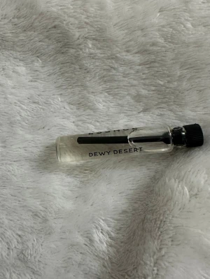 Dewy Desert parfymprov essnce - Litet parfymprov med namnet Dewy Desert. Flaskan är genomskinlig med svart skruvkork och enkel, stilren design. Perfekt att ha med i väskan för att testa en ny doft.