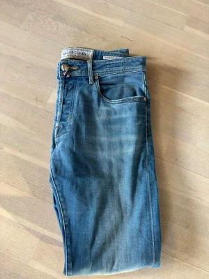 Blå jeans från Jacob Cohen - Snygga blå jeans från Jacob Cohen i klassisk femficksmodell. Jeansen har en rak passform och är tillverkade i mjukt denimtyg med snygga slitningar. Gylfen har knappar och detaljer i kontrastfärg. Perfekta för en trendig och avslappnad look.