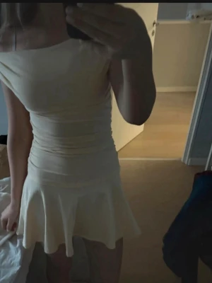 Ljusgul offshoulder kort klänning - Trendig ljusgul kort klänning med offshoulder-design och figurnära passform. Kjolen har en lätt utsvängd volangkant som ger en söt och ungdomlig look. Perfekt för sommarens alla tillfällen. Materialet känns mjukt och stretchigt, troligen bomull eller polyester.