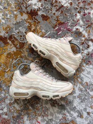 Nike Air Max 95 beige sneakers - Snygga Nike Air Max 95 sneakers i beige med ikoniska vågformade paneler och synlig Air-dämpning i sulan. Skorna har mesh och läderdetaljer, samt diskreta Nike-loggor på sidan och hälen. Perfekta för dig som gillar streetwear och sportig stil.