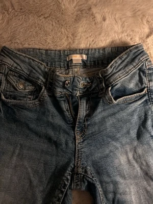 Blå raka jeans med fickdetaljer - Ett par klassiska blå jeans med raka ben och snygga fickdetaljer fram. Jeansen har normalhög midja och dragkedja med knappstängning. Materialet är slitstark denim i bomull. Perfekta för en avslappnad och trendig look.