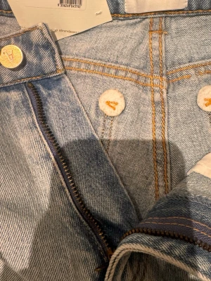 Ljusblå jeans från Abrand - Säljer ett par ljusblå jeans från Abrand med klassisk femficksdesign och guldfärgade detaljer på knappar och dragkedja. Jeansen har raka ben och är tillverkade i slitstark denim med snygga kontrastsömmar. Perfekta för en avslappnad och trendig look.