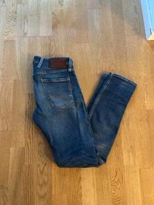 Replay anbass W30 L32 - Säljer ett par blå slim fit jeans från Replay med klassisk femficksdesign och snygga slitningar på framsidan. Jeansen har en mörk tvätt och detaljerade sömmar. Perfekta för dig som gillar en modern och avslappnad stil.