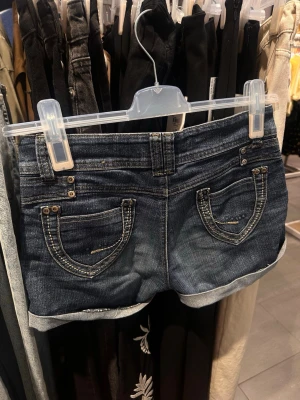 Lågmidjade jeansshorts  - Säljer ett par blå lågmidjade jeansshorts med snygga fickdetaljer. Shortsen har uppvikta benslut och klassisk femficksdesign. Står ingen stolek men skulle säga att de är en S-M. Säljer då de tyvärr är för små.