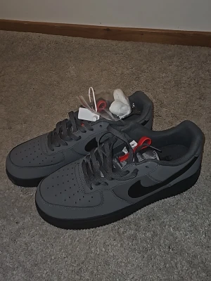 Nike Air Force 1 Low grå/svart - Nike Air Force 1 fick de i present och har aldrig använt de då de är derför jag säljer dom. Kommer även med ett nytt sett skosnören i färg vit