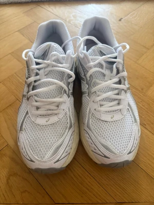 Vita Asics sneakers med mesh - Snygga vita sneakers från Asics med mesh-överdel och silverdetaljer. Skorna har klassisk låg profil, bekväm passform och robust sula. Perfekta för dig som gillar sportig stil och vill ha ett par lätta och ventilerande sneakers.