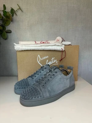 Christian Louboutin Skor/Sneakers Gråa - Snygga gråa sneakers från Christian Louboutin i mocka med matchande grå sula. Skorna har coola nitar på tån och klassisk låg profil. Perfekta för dig som vill sticka ut med exklusiv design och streetkänsla. Perfekt för dig med pondus och klass, otroligt snygga och har knappt använts 10/10 skick. Vi erbjuder endast 10/10 skick och återbetalning vid fel information. Först till kvarn. Dessa finns i 3 olika storlekar kom pm för mer info. OBS alla i samma skick - utseende.