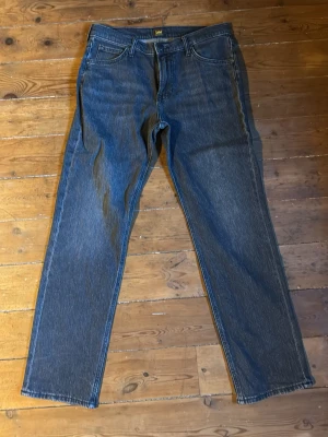 Lee raka grå/svarta jeans - Klassiska svarta jeans från Lee med rak passform och fem fickor. Jeansen har normal midja, dragkedjegylf och är tillverkade i slitstark denim. Perfekta för en avslappnad och tidlös stil.
