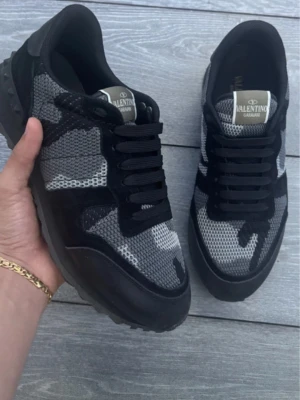 Valentino Garavani camo sneakers - Snygga sneakers från Valentino Garavani med svart och grått camouflagemönster. Skorna har svarta snören, meshdetaljer och svarta mockapartier. Märkeslogga på plösen och robust sula för extra streetkänsla.