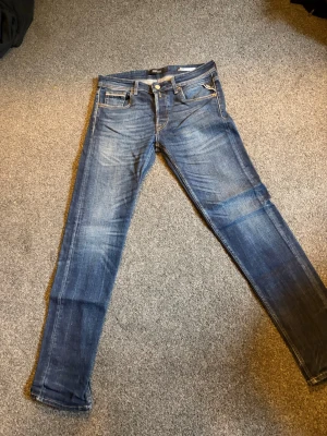 Blå Replay jeans med raka ben - Snygga blå jeans från Replay med raka ben och klassisk femficksdesign. Jeansen har slitningar och ljusare partier framtill samt coola detaljer på bakfickorna. Tillverkade i bomull med en skön passform och normal midja.