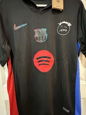 FC Barcelona svart matchtröja Nike - Säljer en svart FC Barcelona matchtröja från Nike med röda och blå detaljer på sidorna. Tröjan har klubbmärke, Spotify-logga och ett unikt grafiskt tryck på bröstet. Tillverkad i lätt polyester, perfekt för fotboll eller träning.
