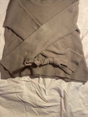 Beige/Lila stickad tröja med knytband - Mysig beige/lila stickad tröja med långa ärmar och dekorativa knytband i ärmarna. Tröjan har rund halsringning och är i storlek xs men är ganska strechig så skulle säga mer s! Perfekt för kyliga dagar eller sena sommar kvällar ❤️(Se sista bilden för färg i mörker)