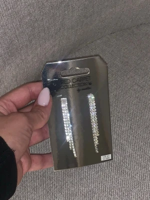 Långa glittriga örhängen Red Carpet - Säljer ett par långa, glittriga örhängen från Red Carpet Collection. Örhängena är silverfärgade och täckta med gnistrande stenar i rad, vilket ger en riktigt lyxig känsla. Perfekta för dig som vill sticka ut och glänsa lite extra.