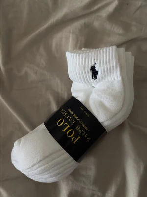 Vita strumpor  - Klassiska vita strumpor från P R L med den ikoniska mörkblå loggan broderad vid ankeln. Strumporna är ribbade upptill och tillverkade i mjuk bomull för skön komfort. Perfekta till sneakers eller loafers. Strumporna passar vem som när det gäller storlek!