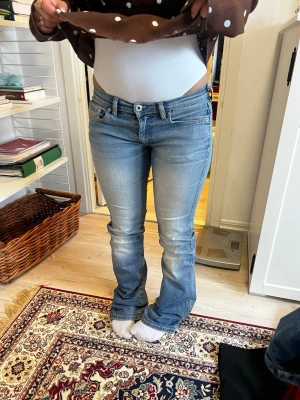 Ljusblå lågmidjade bootcut jeans från Diesel - Snygga ljusblå jeans från Diesel Industry med bootcut-passform och klassiska fem fickor. Jeansen har en låg midja och subtila slitningar framtill för en trendig look. Perfekta för dig som gillar en avslappnad men ändå stilren vibe. Märkesbyxor! Kostar över 1000 nya, stl 26.