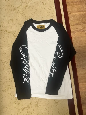 Cortiez long sleeve - Snygg svartvit långärmad t-shirt från Guerillaz med kontrasterande svarta ärmar och grafiskt tryck längs båda ärmarna. Klassisk baseballmodell med rund halsringning och cool streetwear vibe. Perfekt för dig som gillar unik stil.