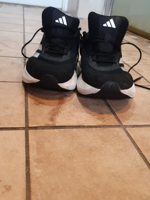Svarta Addidas Spring Skor - Säljer ett par svarta Adidas spring skor med vita detaljer och klassiska ränder på sidorna. Skorna har en sportig design med mesh-ovandel för bra ventilation och en tjock vit sula som ger skön dämpning. Perfekta för träning eller streetwear. Använt dom typ 3-4 gånger, men högra skon har en liten skada typ vid hälen. Hör gärna av er om ni vill ha mer bilder.