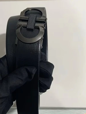 Svart skärp från Salvatore Ferragamo - Snyggt svart skärp från Salvatore Ferragamo med en ikonisk metallspänne i mörk silverfärg. Bältet är gjort i äkta skinn och har en stilren, modern look som passar till många outfits. Perfekt accessoar för att lyfta din stil.