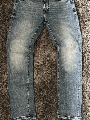 Blå raka jeans - Säljer ett par blå jeans med raka ben och snygga slitningar på framsidan. Jeansen har klassisk femficksdesign och ljus tvätt som ger en avslappnad look. Perfekta till vardags för en cool och enkel stil.
