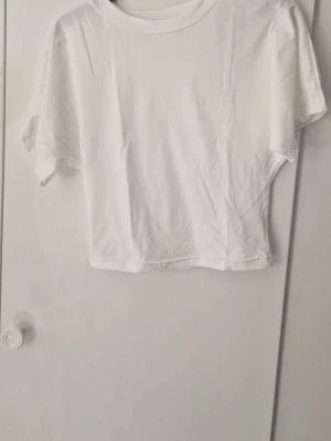 Vit croppad t-shirt i bomull - En enkel och stilren vit croppad t-shirt med rund hals och korta ärmar. Perfekt basplagg som passar till allt och är lätt att matcha. Tillverkad i mjuk bomull för en skön känsla. Den är från Temu och är en magtröja och är väldigt kort och liten
