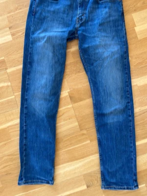 Blå raka jeans från Levi's - Klassiska blå jeans från Levi's med rak passform och fem fickor. Jeansen har en snygg tvätt med lätt slitning på låren och bakfickor med den ikoniska Levi's-sömmen. Perfekta till en avslappnad stil.
