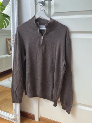  Stickad halvzip från Bläck strl M - Mysig stickad tröja från Bläck med halvzip och hög krage. Tröjan har långa ärmar och ribbade muddar vid ärmslut och nederkant. Perfekt för lager på lager och enkel att matcha med jeans eller chinos. 100% bomull 