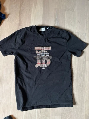 Svart Burberry t-shirt med logga - Svart t-shirt från Burberry med klassisk rund hals och korta ärmar. Stor logga med Burberry-tryck i beige, rött och svart på bröstet. Perfekt för dig som gillar stilrena plagg med exklusiv känsla. Sitter som M