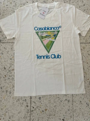 Casablanca Tennis Club - vit/blå t shirt. - Säljer en vit t-shirt från Casablanca med färgglatt tryck och texten 'Casablanca Tennis Club' på bröstet. Oanvänd med original tags som medföljer. Tveka inte på att höra av dig vid funderingar.