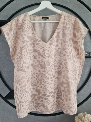 Beige leopardmönstrad topp KappAhl - Snygg beige topp från KappAhl med leopardmönster och v-ringning. Modellen är ärmlös och har en lös passform, perfekt för en trendig och avslappnad look.