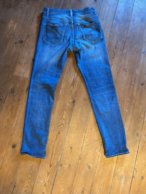 Blå slim fit jeans med slitningar - Snygga blå slim fit jeans med lätt slitna detaljer och klassisk femficksdesign. Jeansen har normalhög midja och smala ben. Materialet är denim i bomull med lite stretch för skön passform. Perfekta till en avslappnad stil.