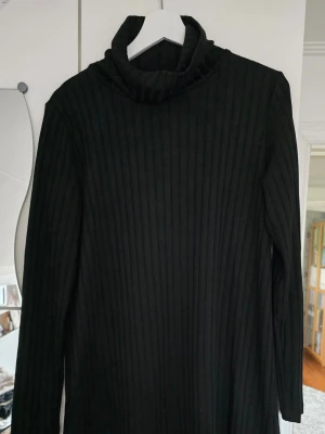 Svart ribbstickad poloklänning Gina Tricot - Svart ribbstickad poloklänning från Gina Tricot. Kort A-linje klänning med lång ärm, hög polokrage och är tillverkad i mjukt, stretchigt material. Perfekt för lager-på-lager och enkel att matcha med olika outfits. 