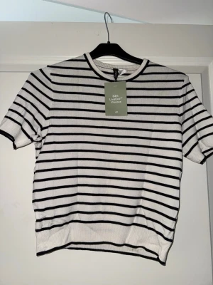 Vit/ svart randig T-shirt - Vit/ svart randig T-shirt från H&M, kortare modell. Lappen är kvar, oanvänd.