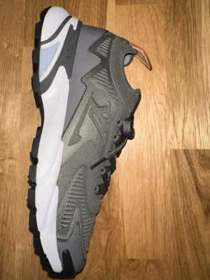Gråa Lv tatic - Snygga gråa lv tatic sneakers med chunky vit sula och svarta detaljer. Ovandelen är i mesh och syntetmaterial för bra andningsförmåga och komfort. Skorna har en modern design med mjuk yttersula och klassisk snörning. Perfekta för dig som gillar streetwear.