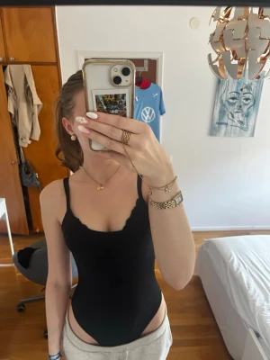 Svart body med smala axelband - Säljer en stilren svart body med smala axelband och rundad urringning. Bodyn har en enkel och klassisk design som passar till många olika outfits. Materialet är stretchigt och följsamt för en bekväm passform. Passar mig som har S/M