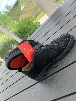 Svarta Christian Louboutin skor med nitar - Säljer ett par svarta skor från Christian Louboutin i mocka med svarta nitar på tån och den ikoniska röda sulan. Skorna har lågt skaft, svarta skosnören och en riktigt lyxig och edgy look. Skorna har blivit använda ett fåtal gånger. Pris kan diskuteras!